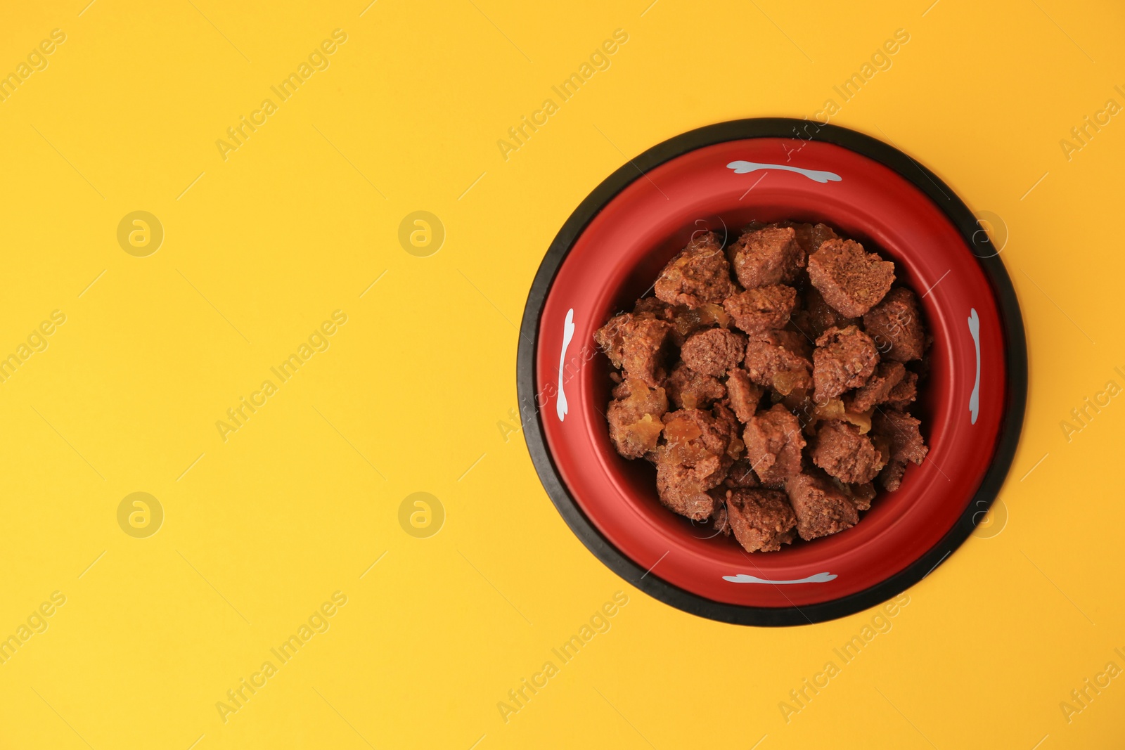 Photo of Wet pet food in feeding bowl on yellow background, top view. Space for text
