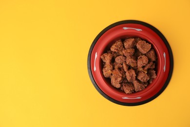 Wet pet food in feeding bowl on yellow background, top view. Space for text