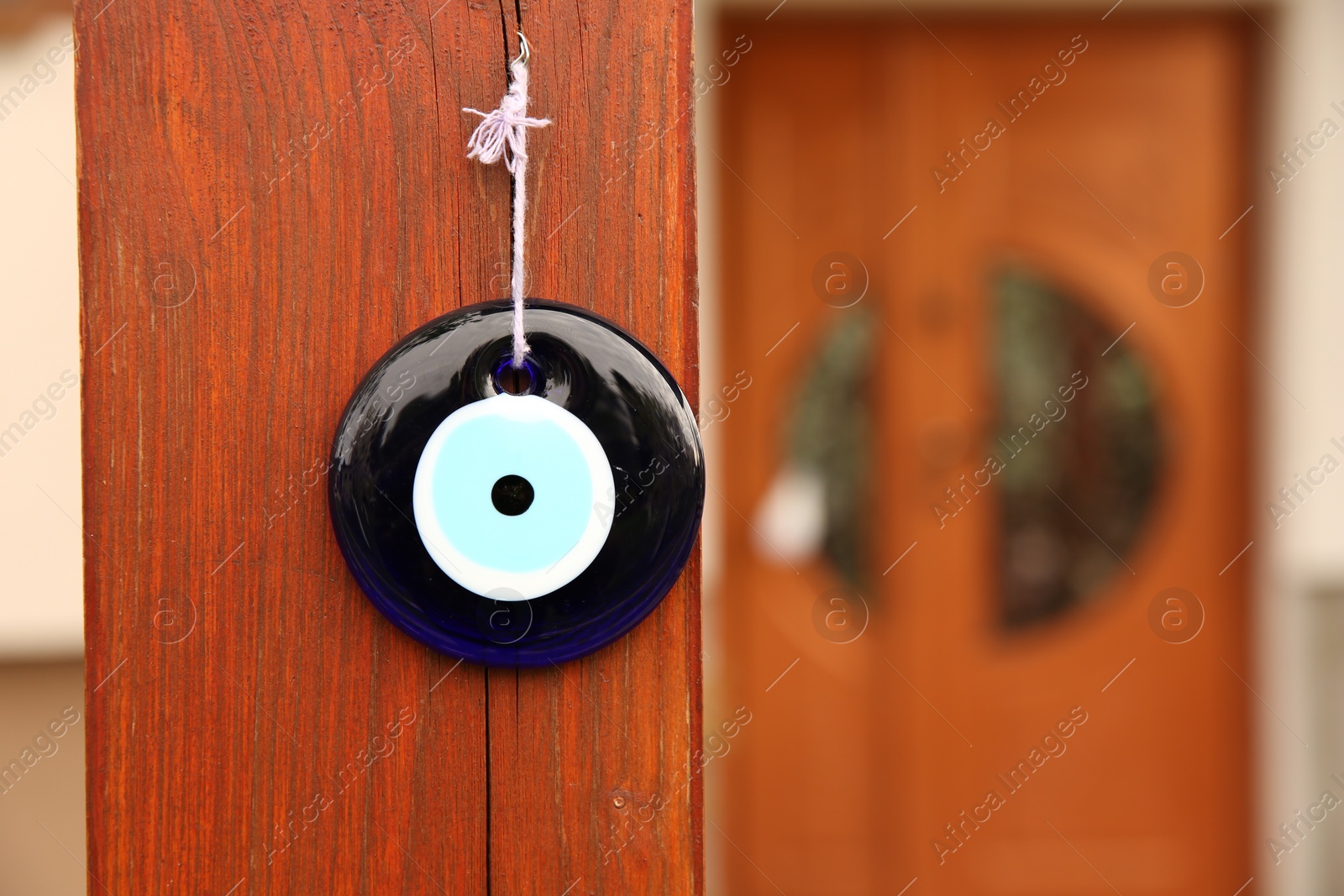 Photo of Evil eye amulet hanging on wooden pillar outdoors, closeup. Space for text