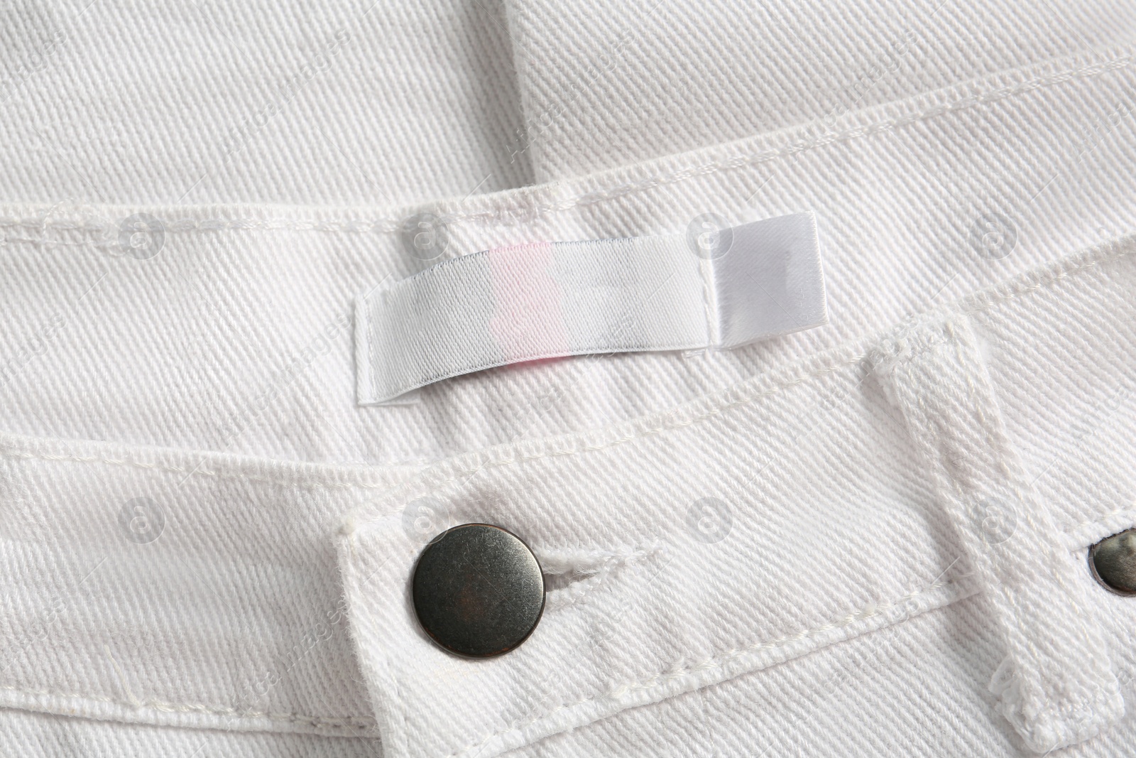 Photo of Blank clothing label on white jeans, top view