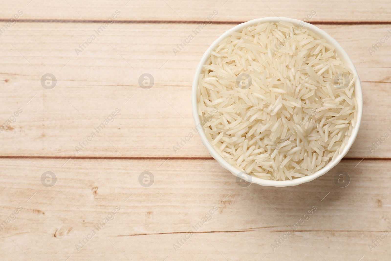 Photo of Raw basmati rice in bowl on white wooden table, top view. Space for text