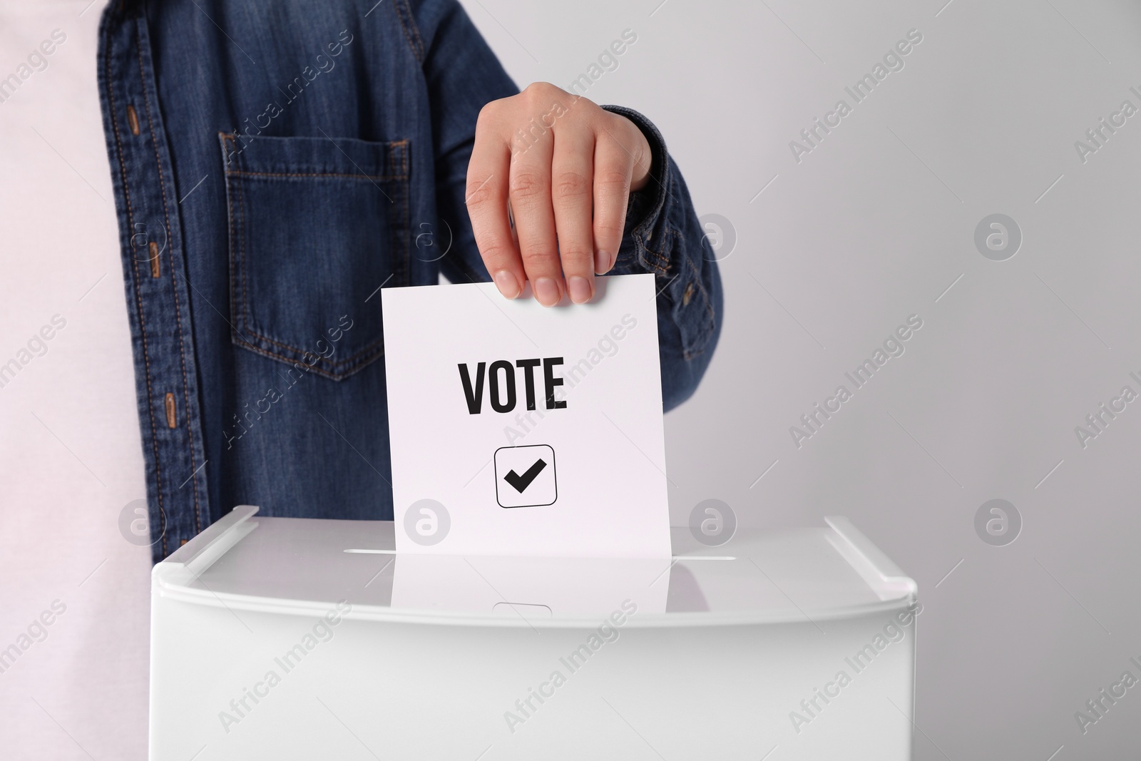 Image of Woman putting paper with word Vote and tick into ballot box on light grey background
