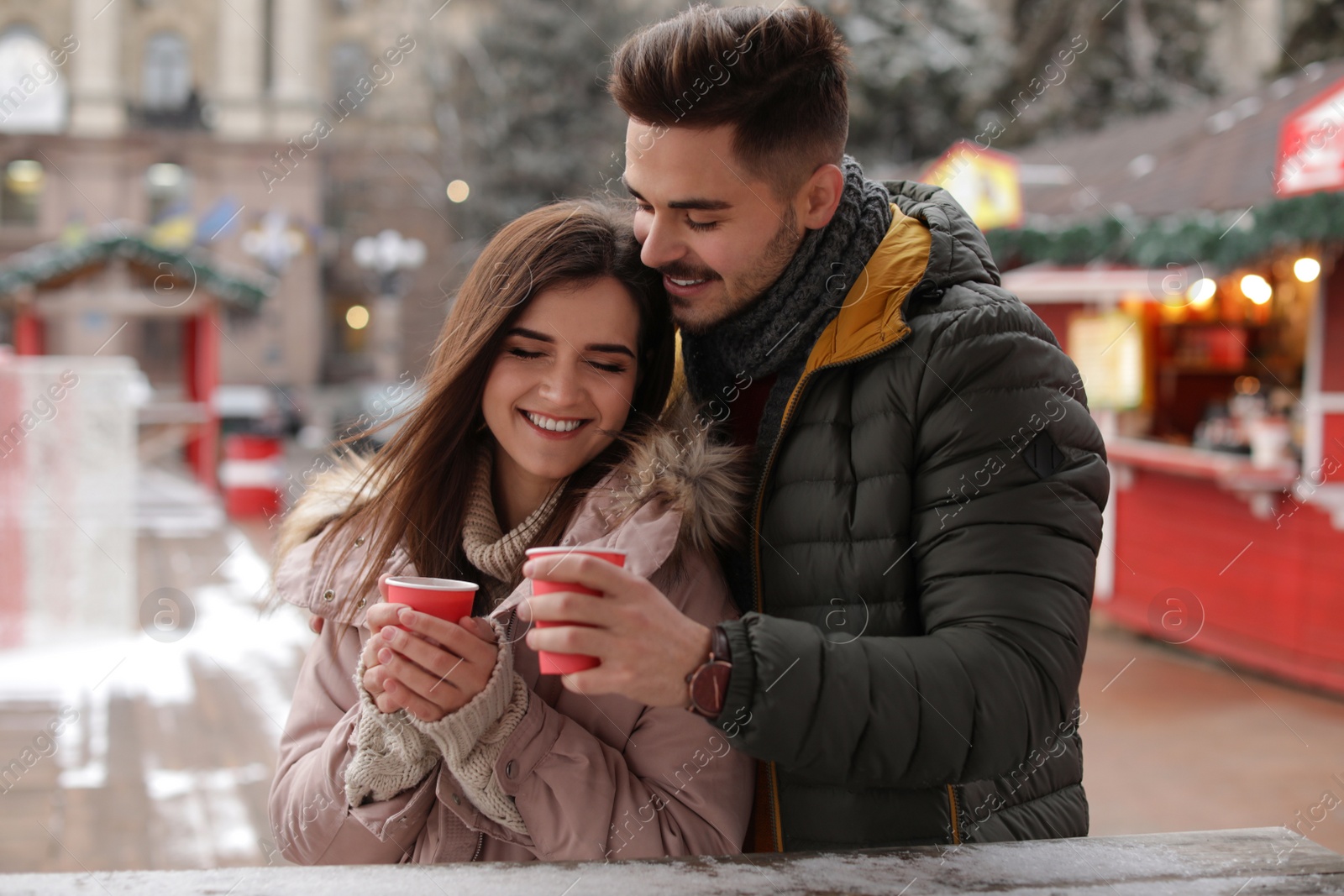 Photo of Young couple with cups of mulled wine at winter fair