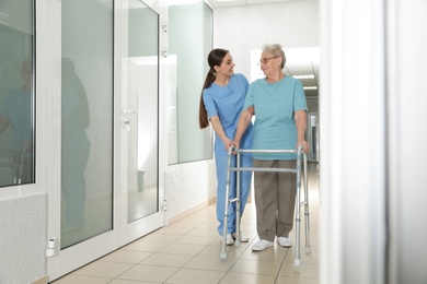 Photo of Nurse assisting senior patient with walker in hospital hallway