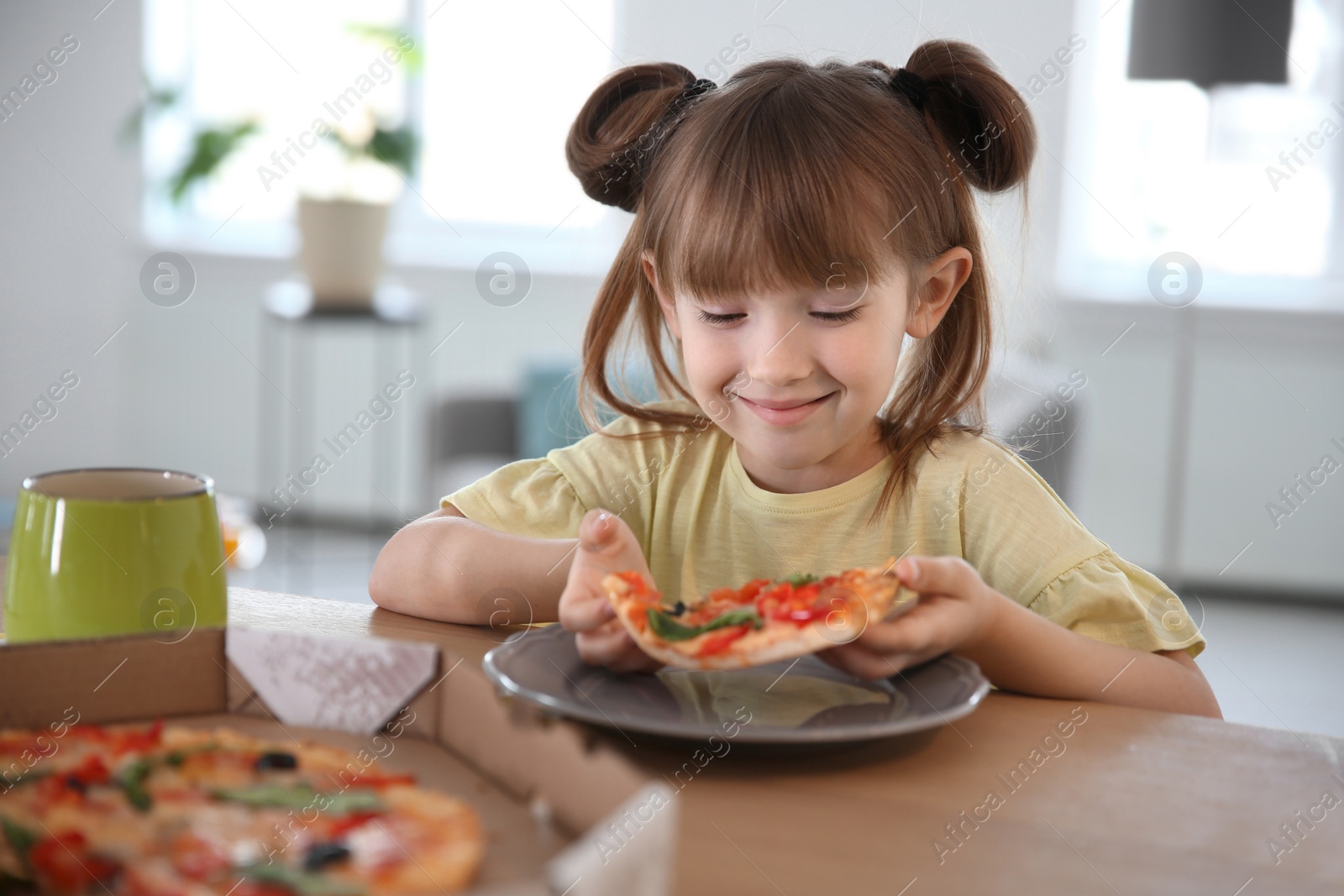 Photo of Cute little girl eating tasty pizza at home