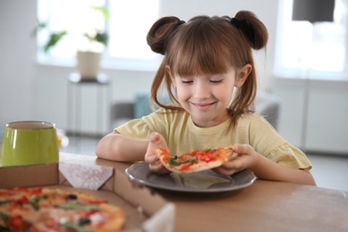 Cute little girl eating tasty pizza at home