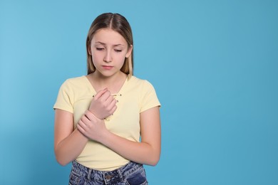 Photo of Teenage girl suffering from pain in wrist on light blue background, space for text. Arthritis symptom