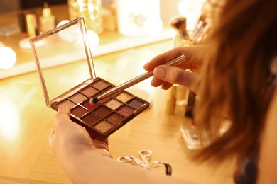 Photo of Woman with eyeshadow palette and brush at dressing table, closeup