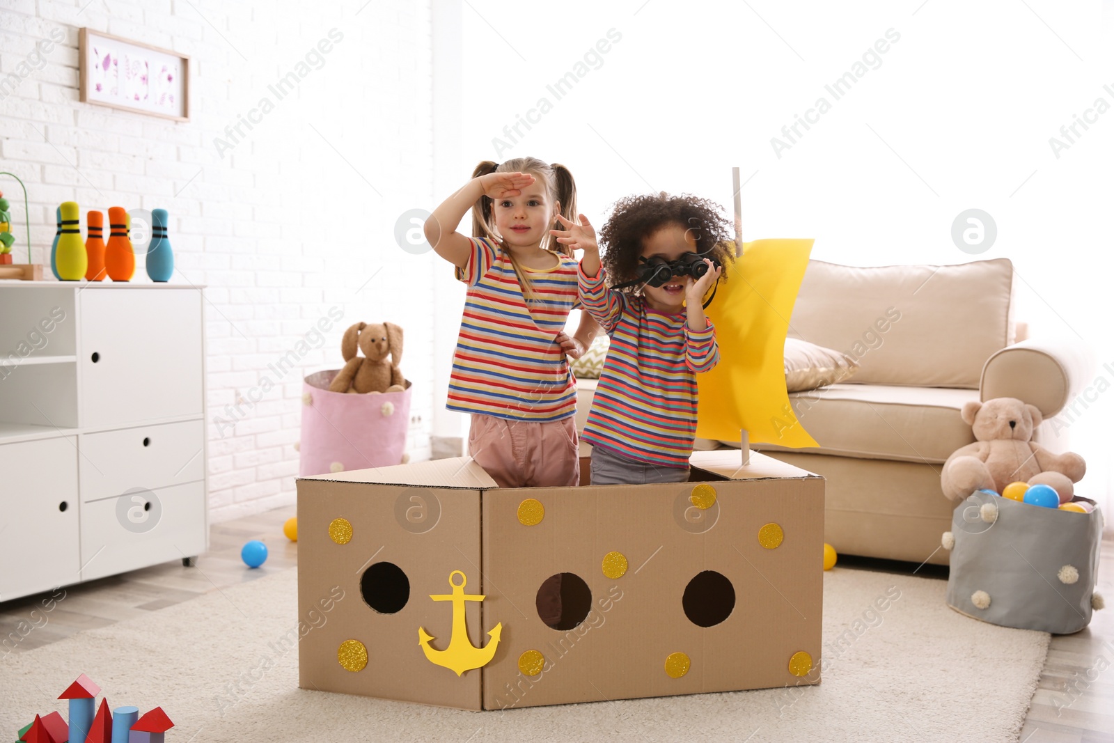 Photo of Cute little children playing with cardboard ship and binoculars at home