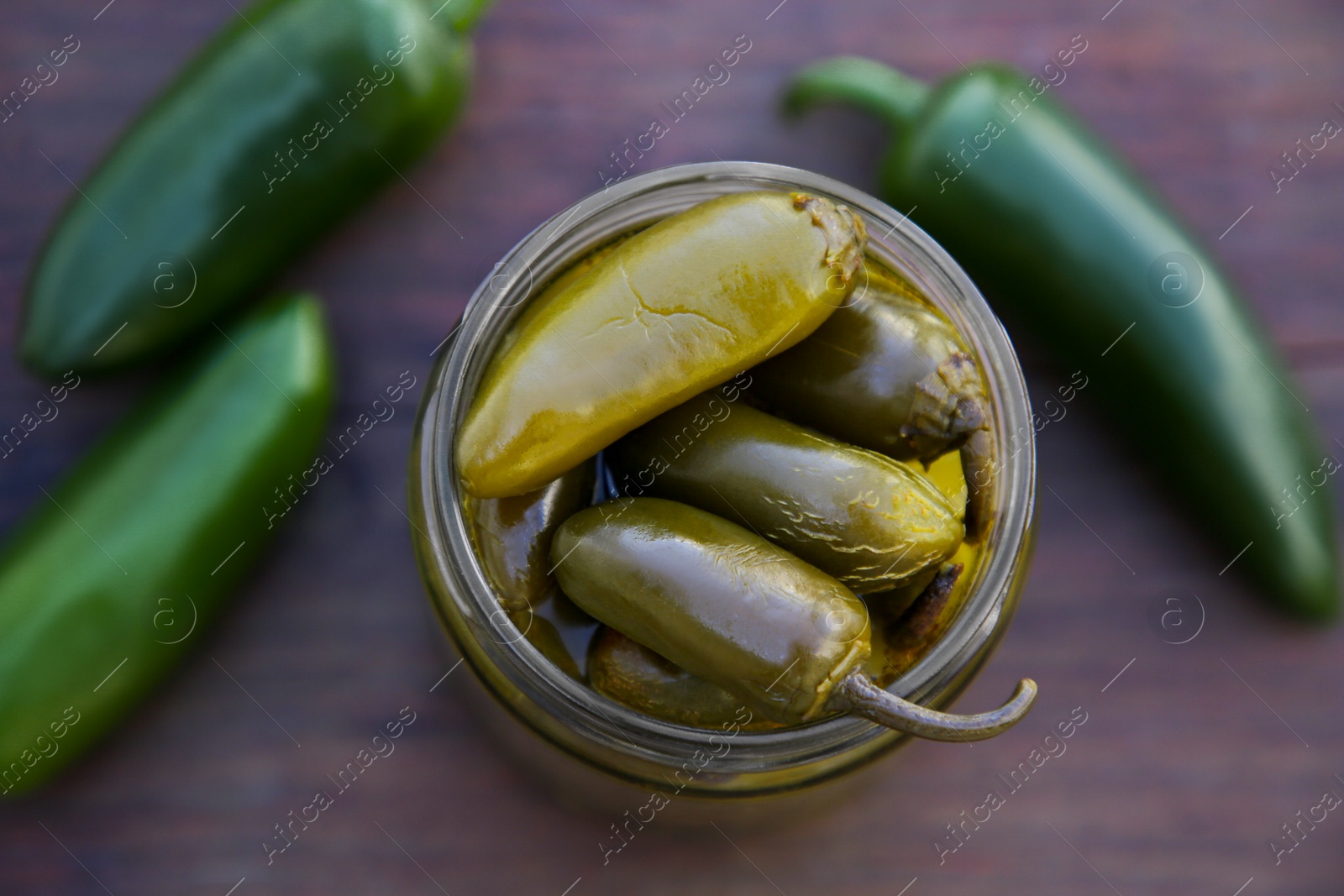 Photo of Fresh and pickled green jalapeno peppers on wooden table, top view