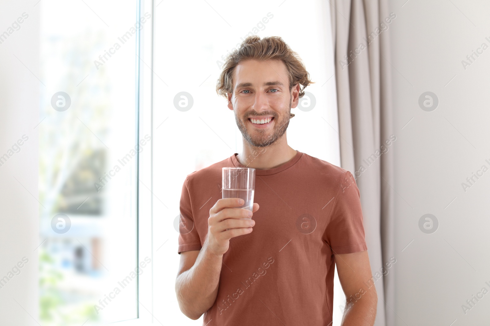 Photo of Young man holding glass of clean water indoors