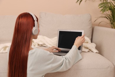 Woman with red dyed hair in headphone using laptop indoors