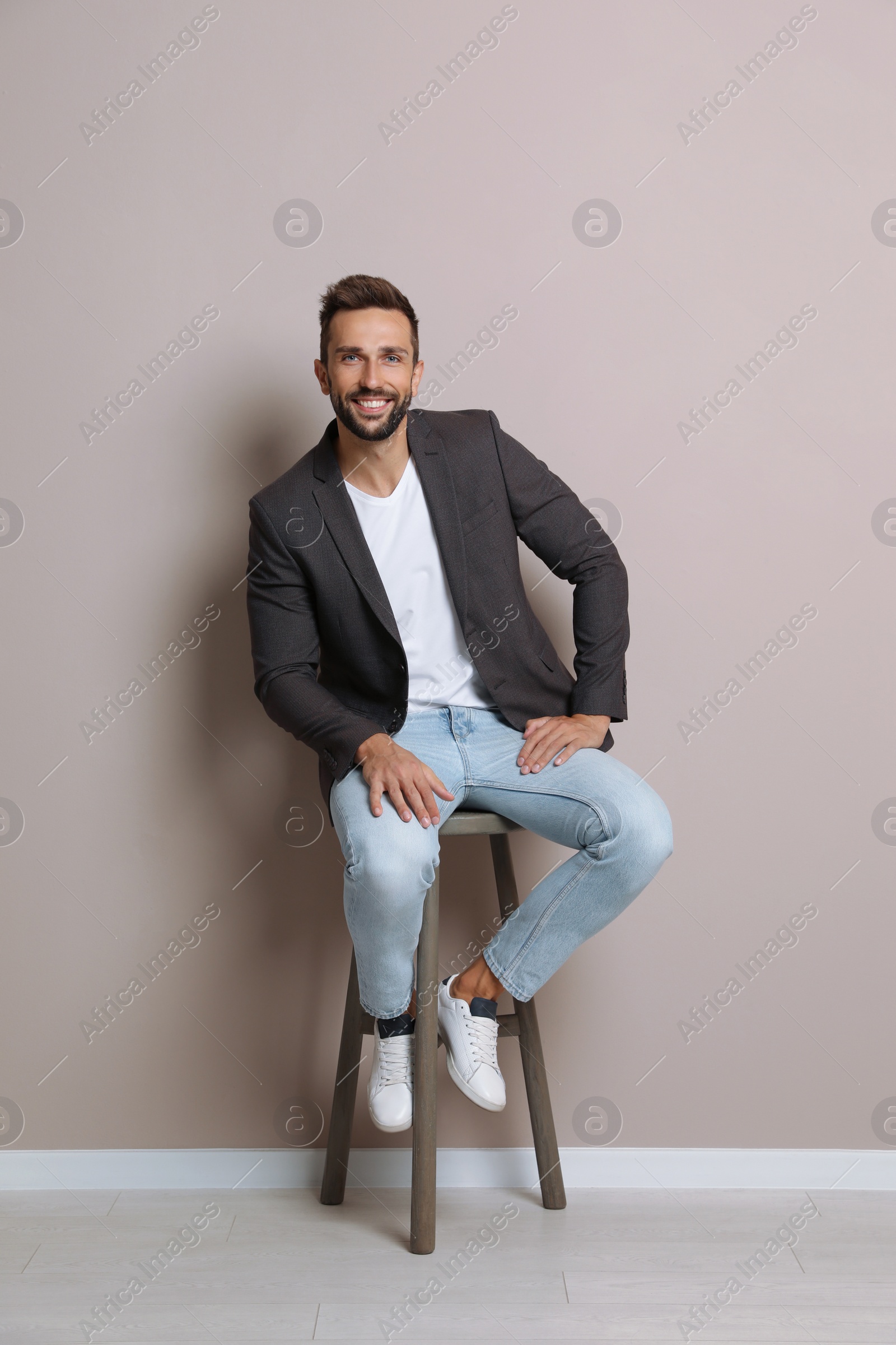 Photo of Handsome man sitting on stool near beige wall