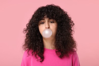 Photo of Beautiful young woman blowing bubble gum on pink background
