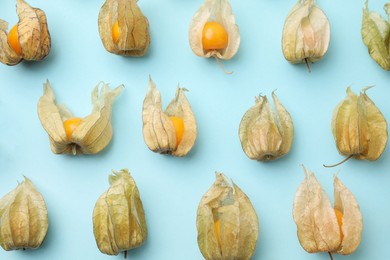 Photo of Ripe physalis fruits with calyxes on light blue background, flat lay