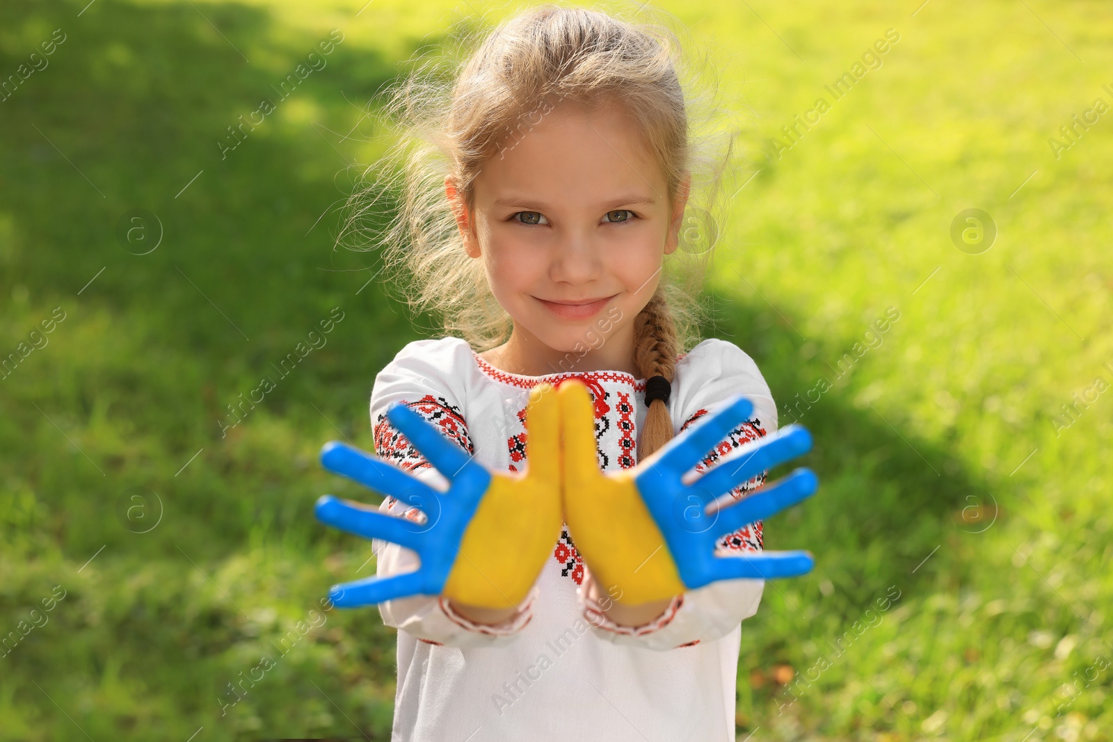 Photo of Little girl with hands painted in Ukrainian flag colors outdoors. Love Ukraine concept