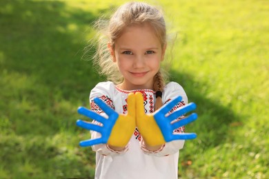 Photo of Little girl with hands painted in Ukrainian flag colors outdoors. Love Ukraine concept