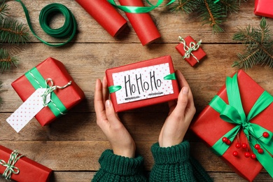 Photo of Woman holding Christmas gift box at wooden table, top view