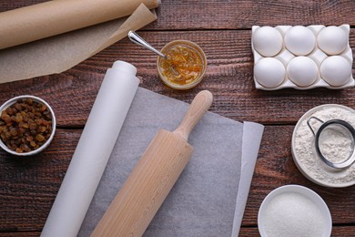 Rolls of baking parchment paper and ingredients on wooden table, flat lay