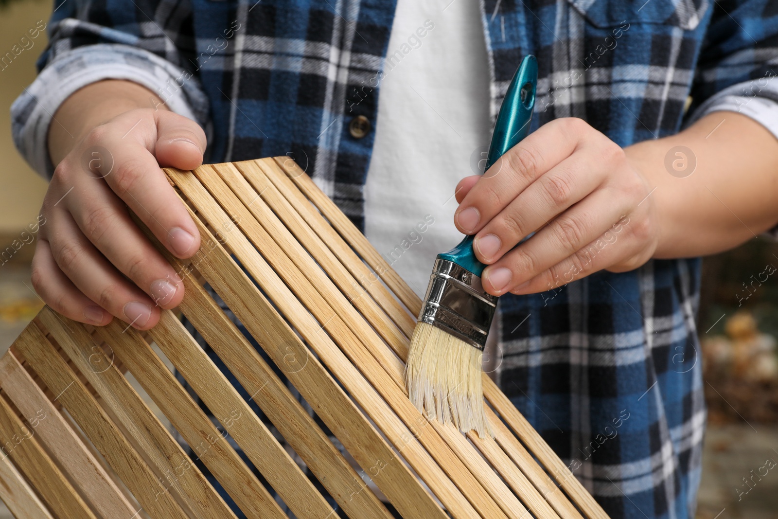 Photo of Man applying varnish onto wooden crate against blurred background, closeup