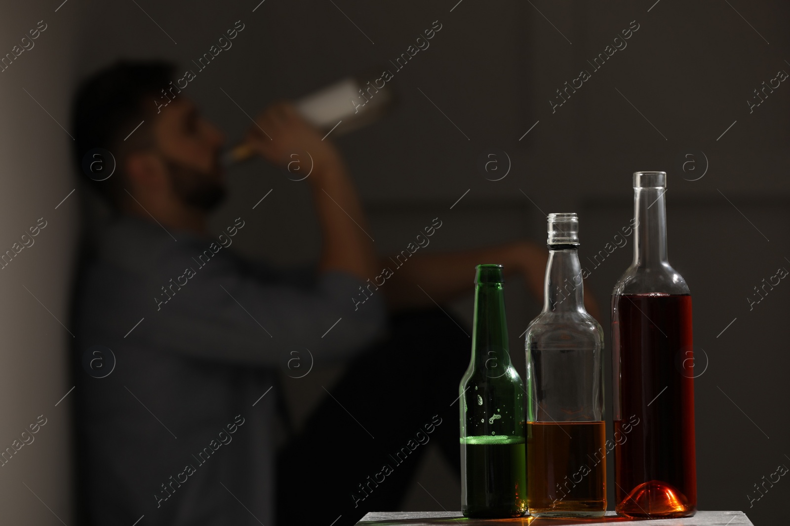 Photo of Addicted man sitting near wall indoors, focus on table with alcoholic drinks. Space for text