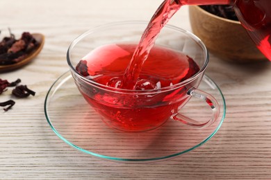 Photo of Pouring fresh hibiscus tea into cup on wooden table, closeup