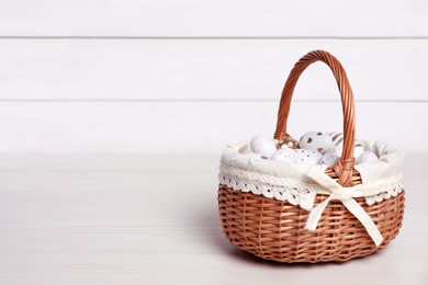 Photo of Wicker basket with festively decorated Easter eggs on white wooden table. Space for text