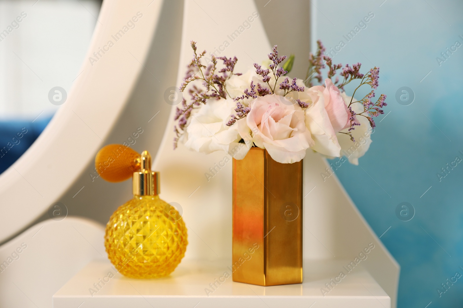 Photo of Bottle of perfume and fresh flowers on dressing table