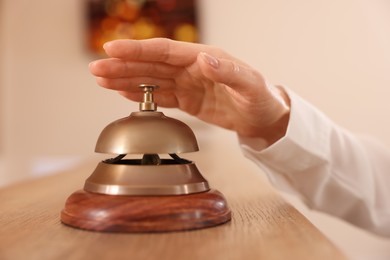 Woman ringing hotel service bell at wooden reception desk, closeup