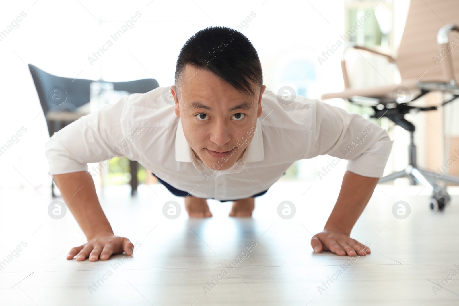 Photo of Young businessman doing exercises in office. Workplace fitness