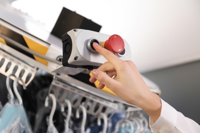 Photo of Worker pressing button on control panel of garment conveyor at modern dry-cleaner's, closeup