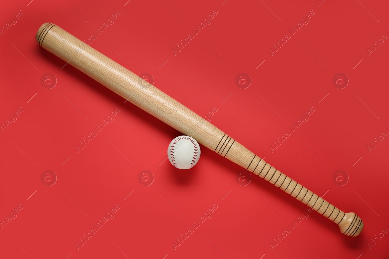 Photo of Wooden baseball bat and ball on red background, flat lay. Sports equipment