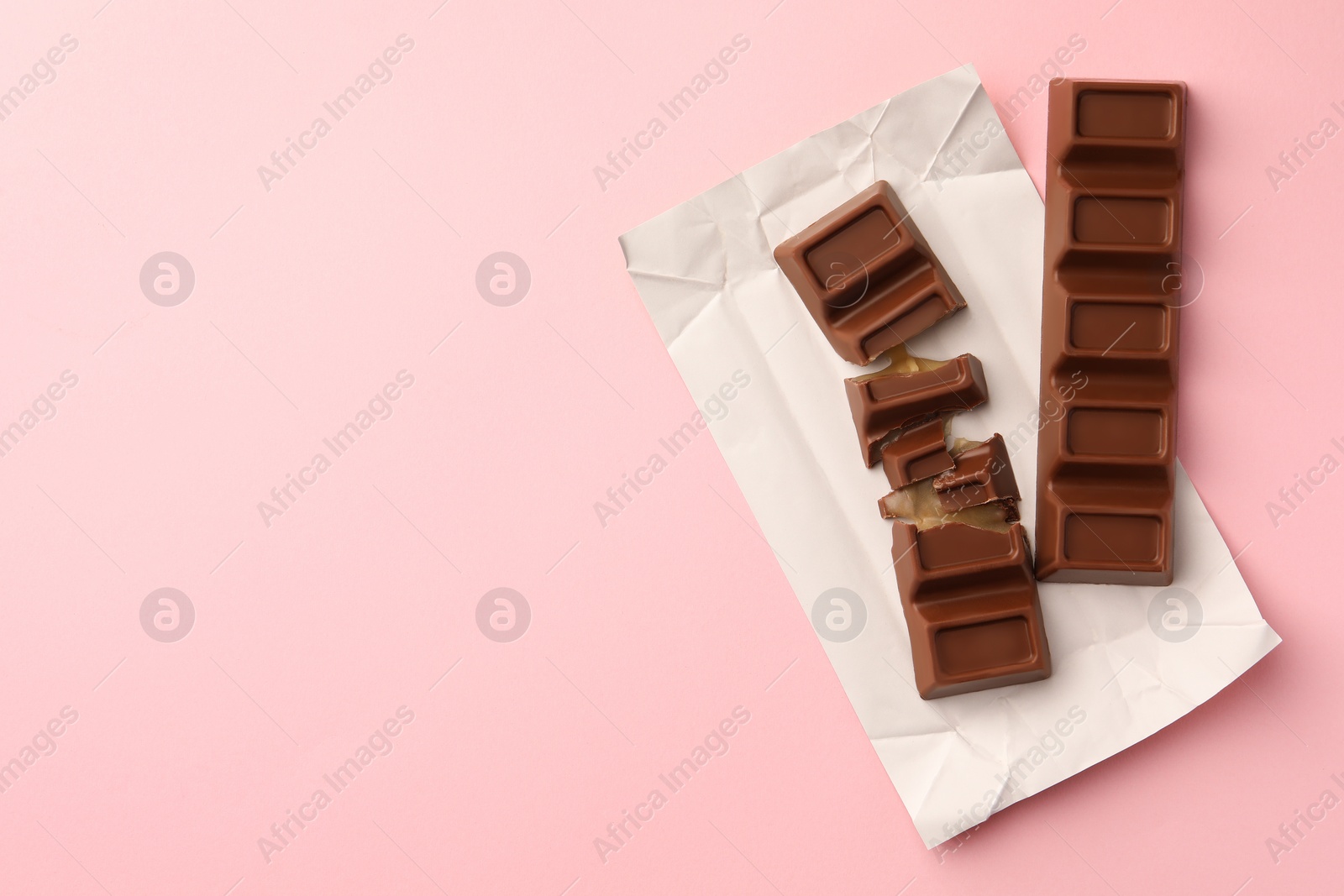 Photo of Paper wrap with delicious chocolate bars on pink background, top view. Space for text