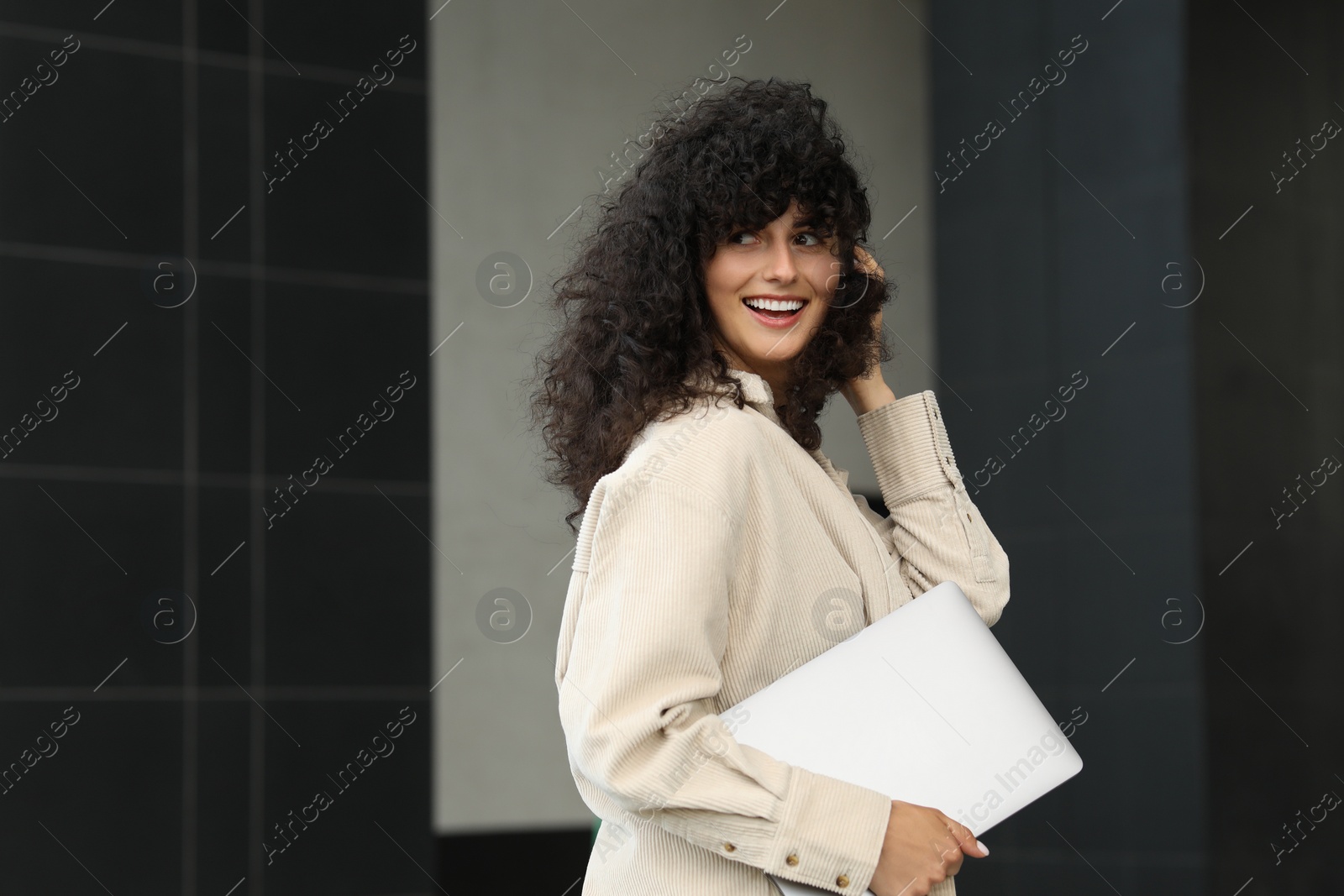 Photo of Happy young woman holding modern laptop outdoors