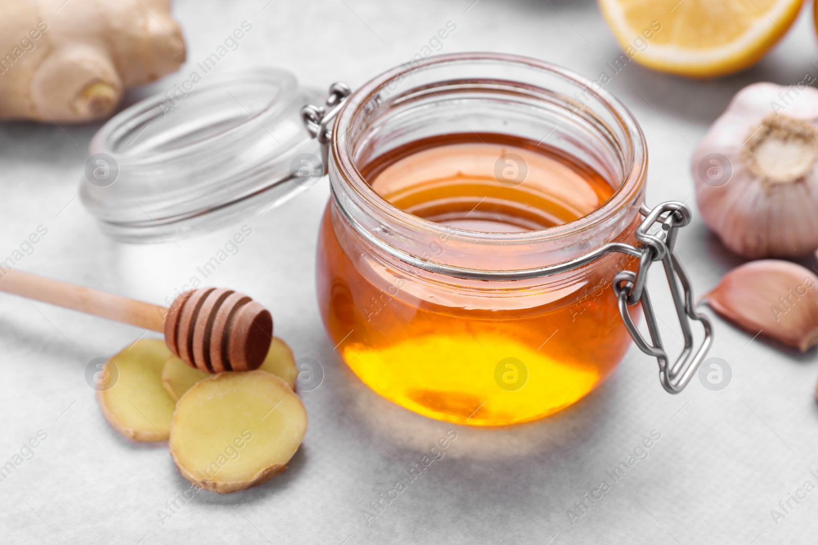 Photo of Natural cough remedies. Jar with honey and ginger on light grey table, closeup