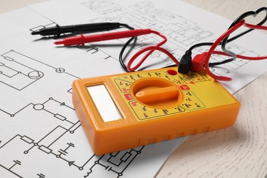 Photo of Wiring diagrams and digital multimeter on white wooden table, closeup