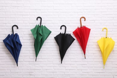 Photo of Closed bright umbrellas hanging on white brick wall