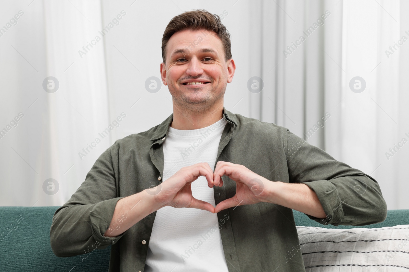 Photo of Happy man making heart with hands at home