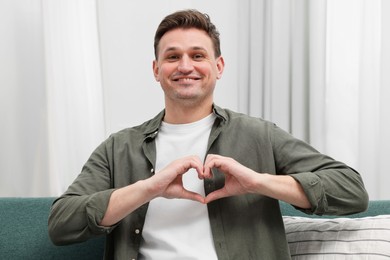 Happy man making heart with hands at home