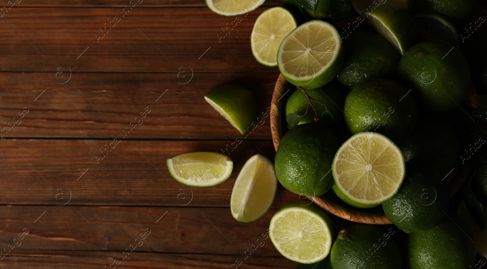 Photo of Fresh whole and cut limes with water drops on wooden table, flat lay. Space for text