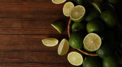 Photo of Fresh whole and cut limes with water drops on wooden table, flat lay. Space for text