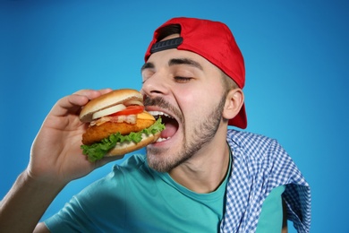 Handsome man eating tasty burger on color background