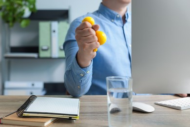 Photo of Man squeezing antistress ball while working with computer in office, closeup