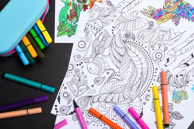 Photo of Antistress coloring pages and felt tip pens on black table, flat lay