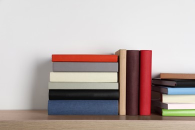 Photo of Many hardcover books on wooden table near white wall