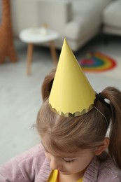 Photo of Cute little girl wearing party hat at home