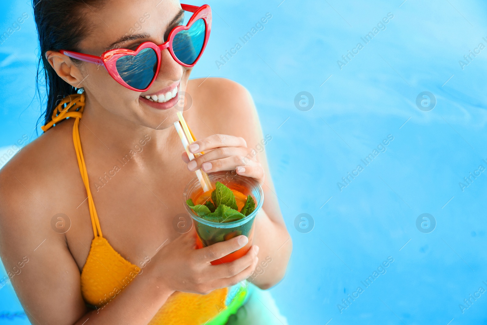Photo of Woman with glass of refreshing drink in swimming pool, closeup