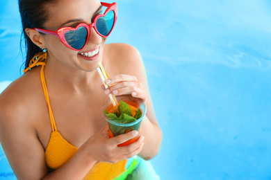 Woman with glass of refreshing drink in swimming pool, closeup