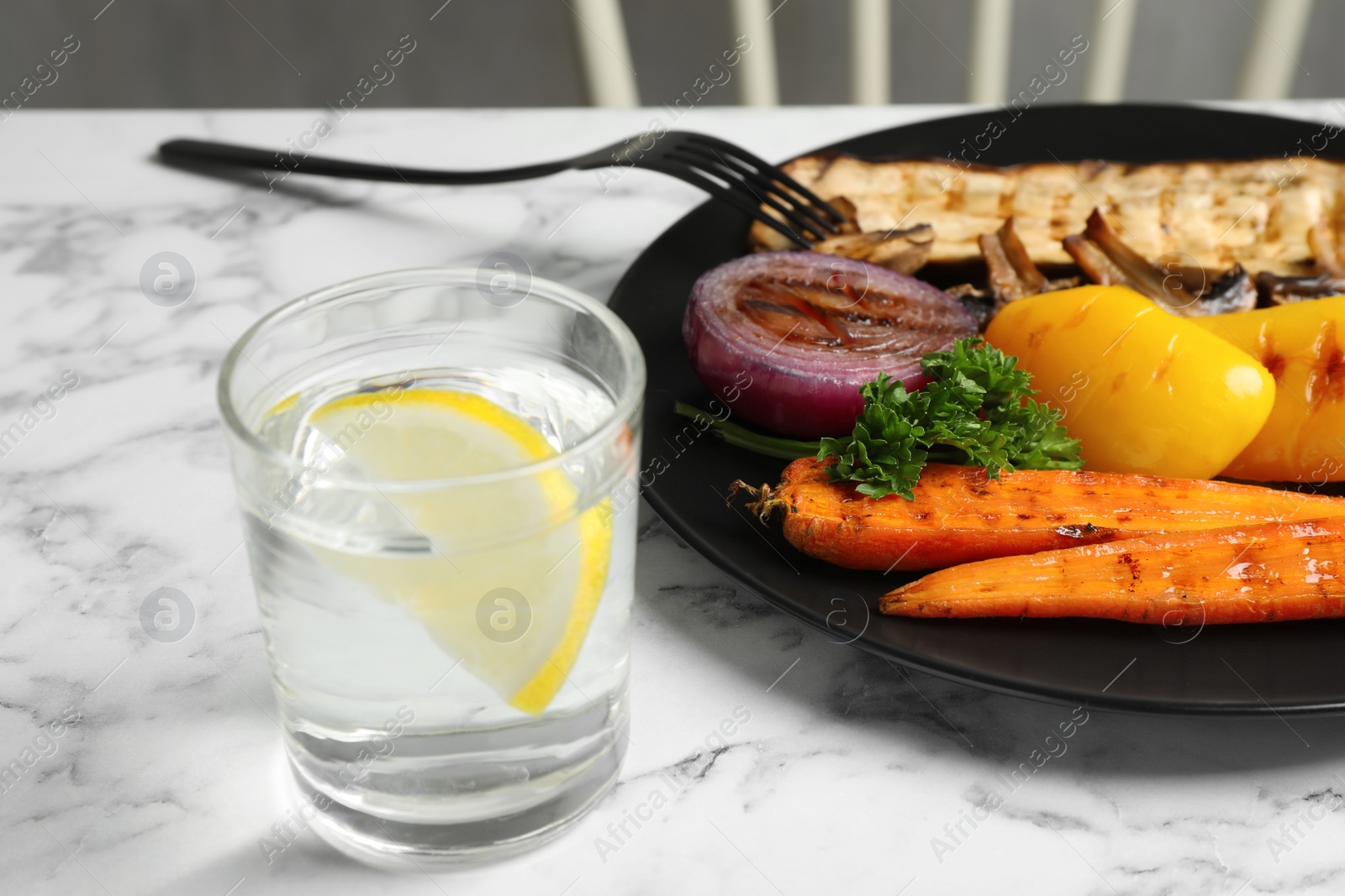Photo of Delicious grilled vegetables and glass of water on white marble table