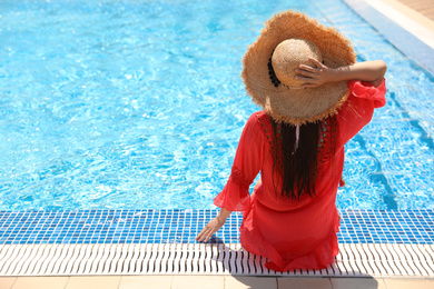 Young woman sitting near outdoor swimming pool, back view. Space for text